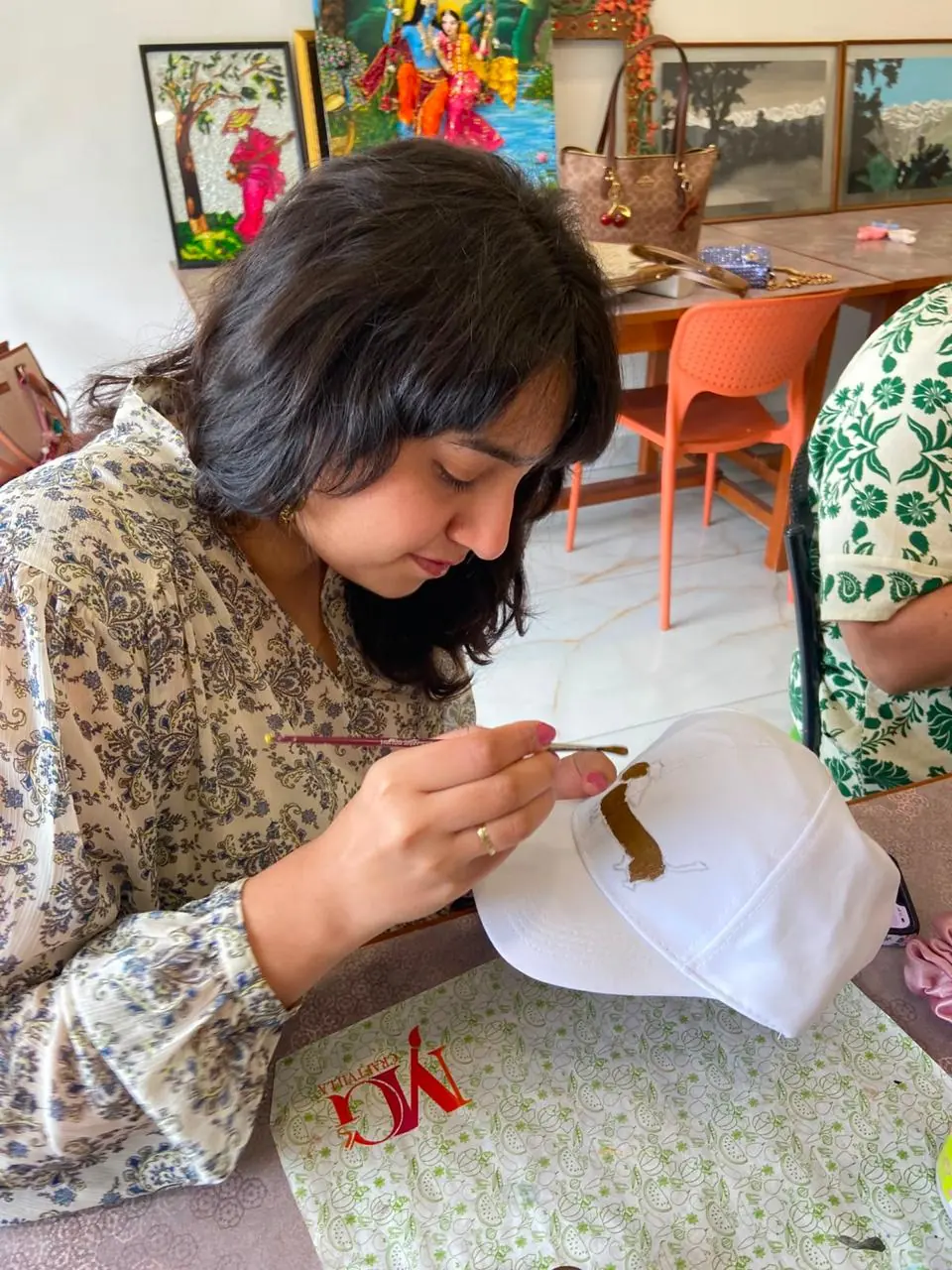 A guest at a Coffee with Canvas session hand-painting a design onto a white cap