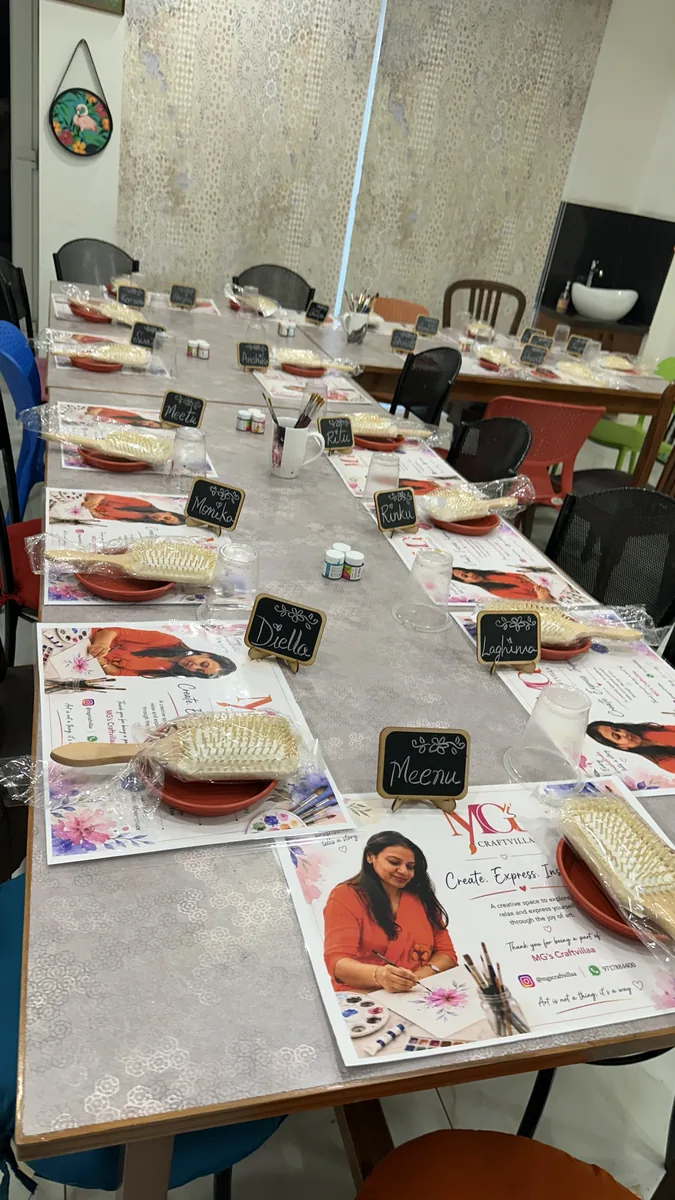 The long studio table laid out before a workshop, with named place cards, paint pots, brushes and a wooden hairbrush at every seat